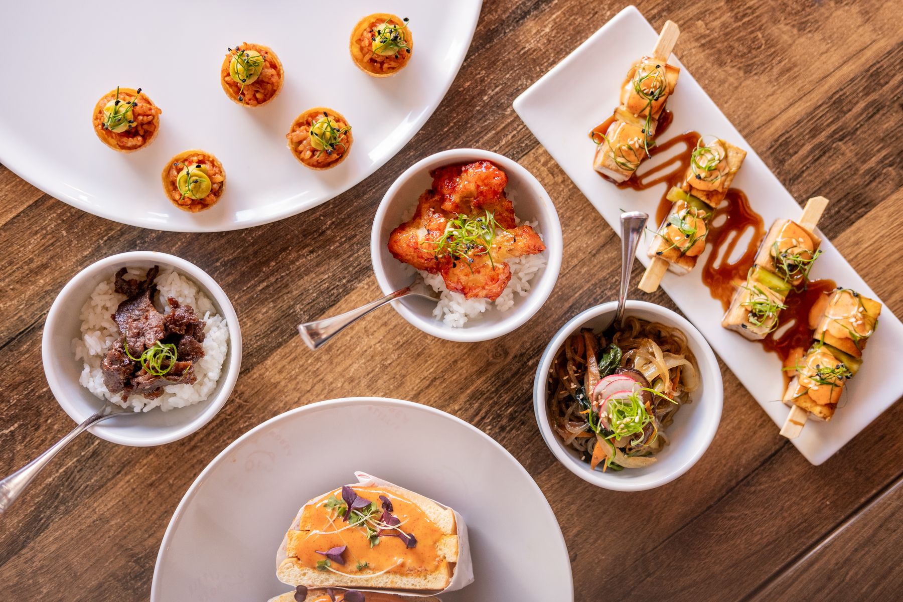 Overhead view of Little Korea canapés, bowl food and skewers on a wooden table